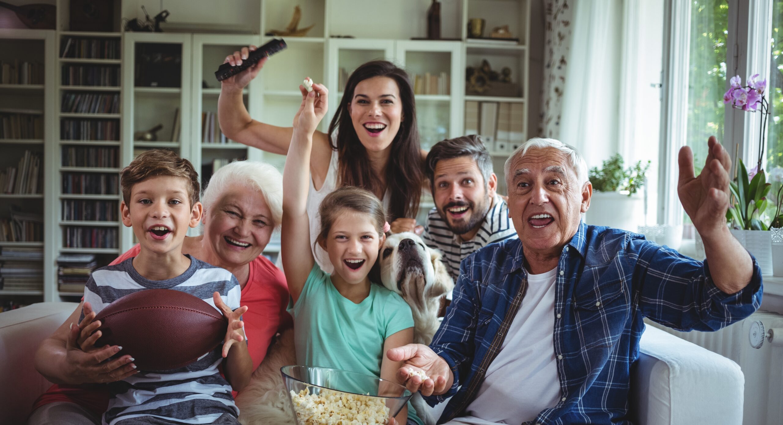 A family celebrates together from their living room couch with a bowl of popcorn.