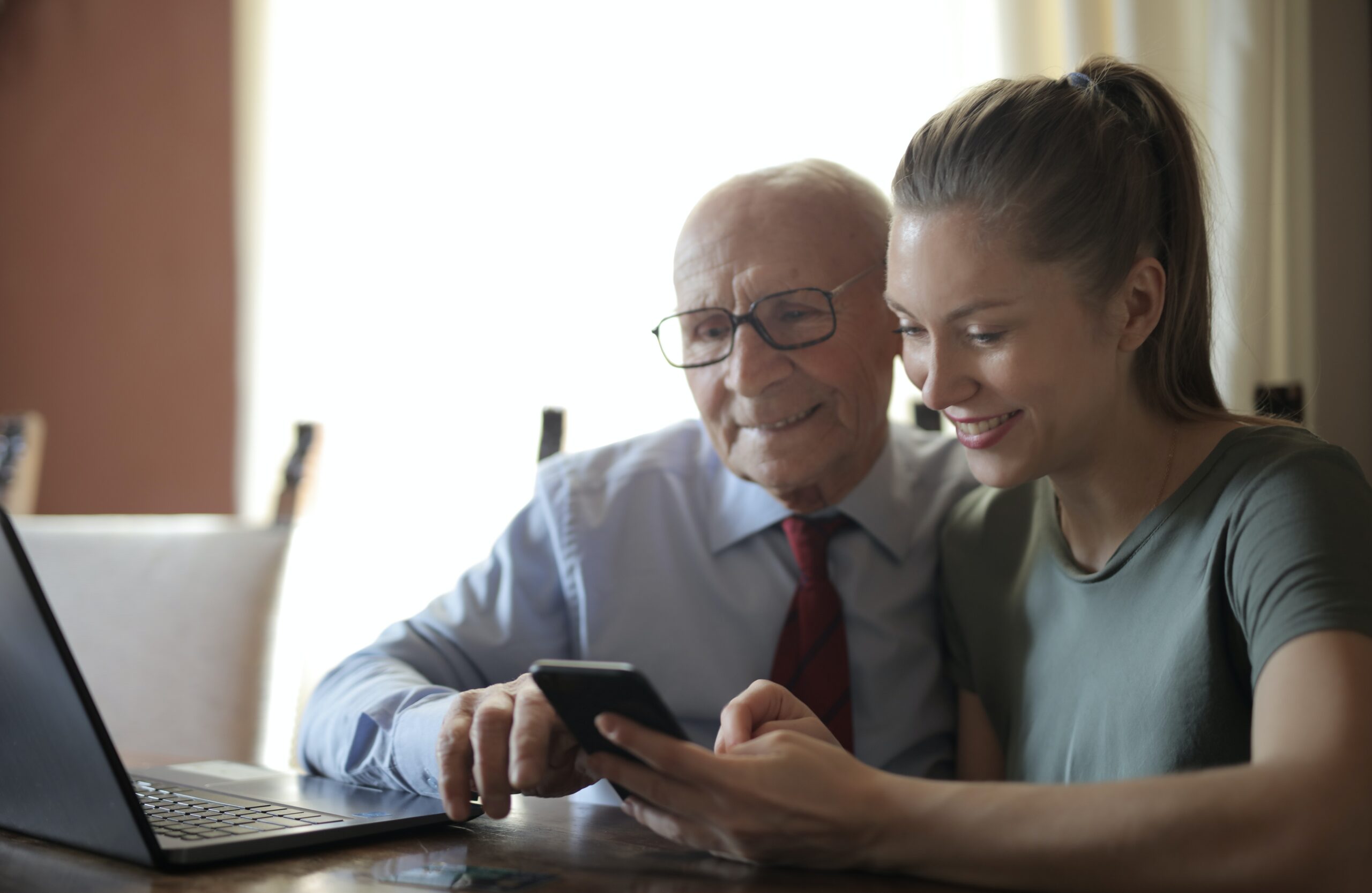 An older man and a young woman look at a smart phone together and smile
