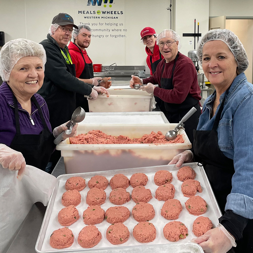 Workers and volunteers smile as they package senior meals.