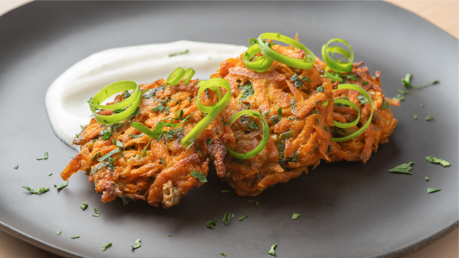 Carrot fritters with herb yogurt on black plate.