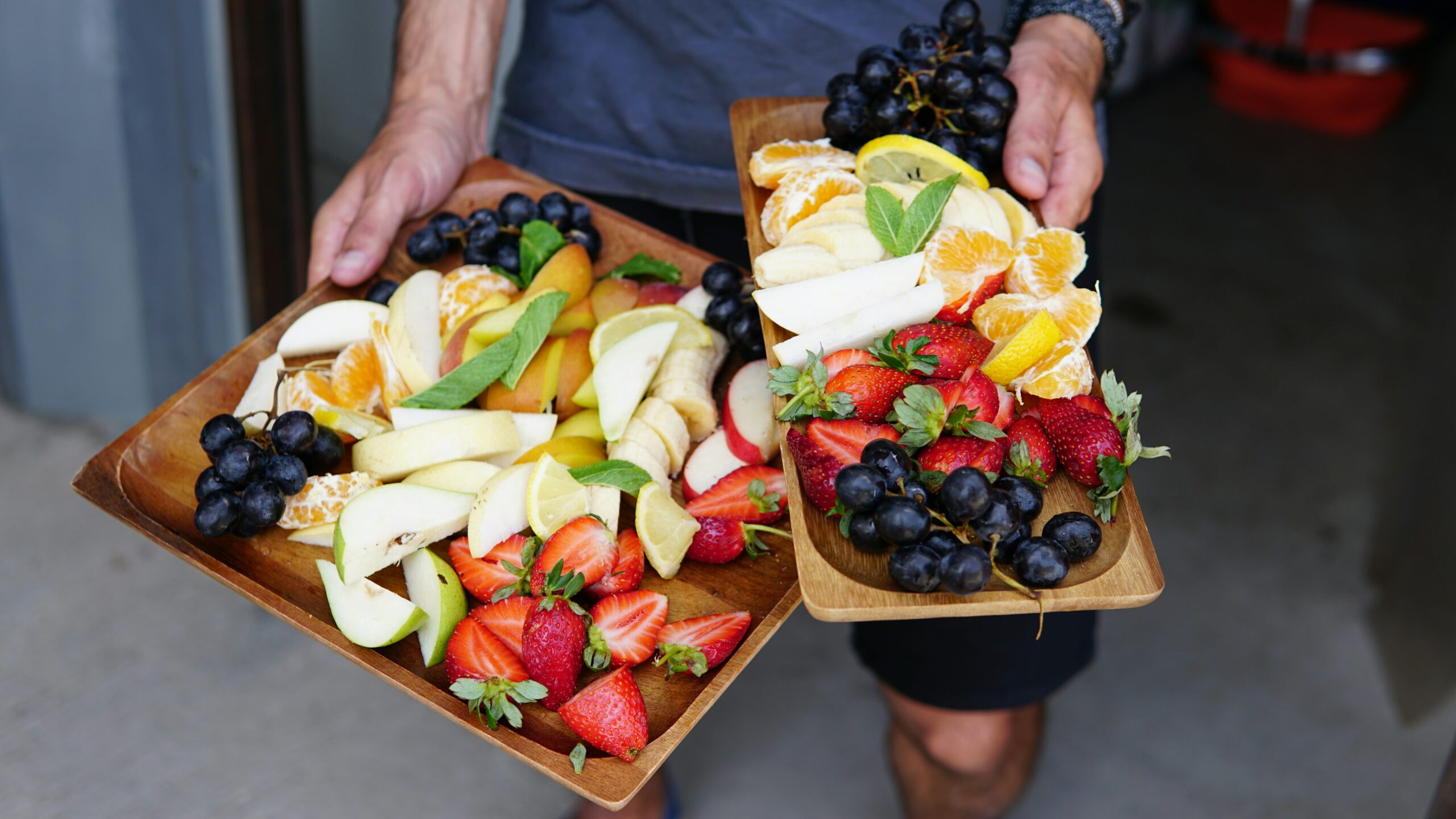 Person holding two trays of fresh-cut, colorful food.