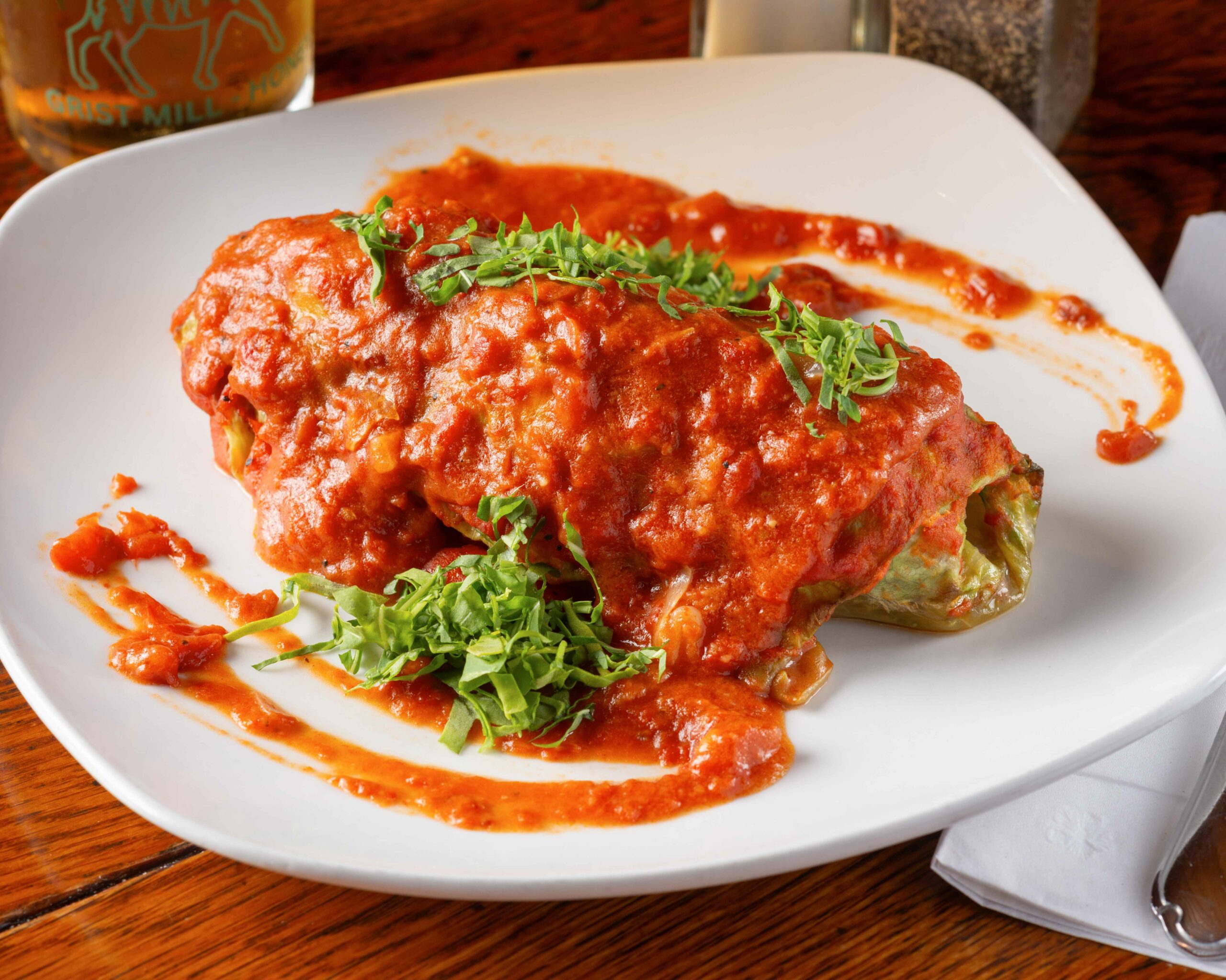 A cabbage egg roll covered in red sauce on a white plate.