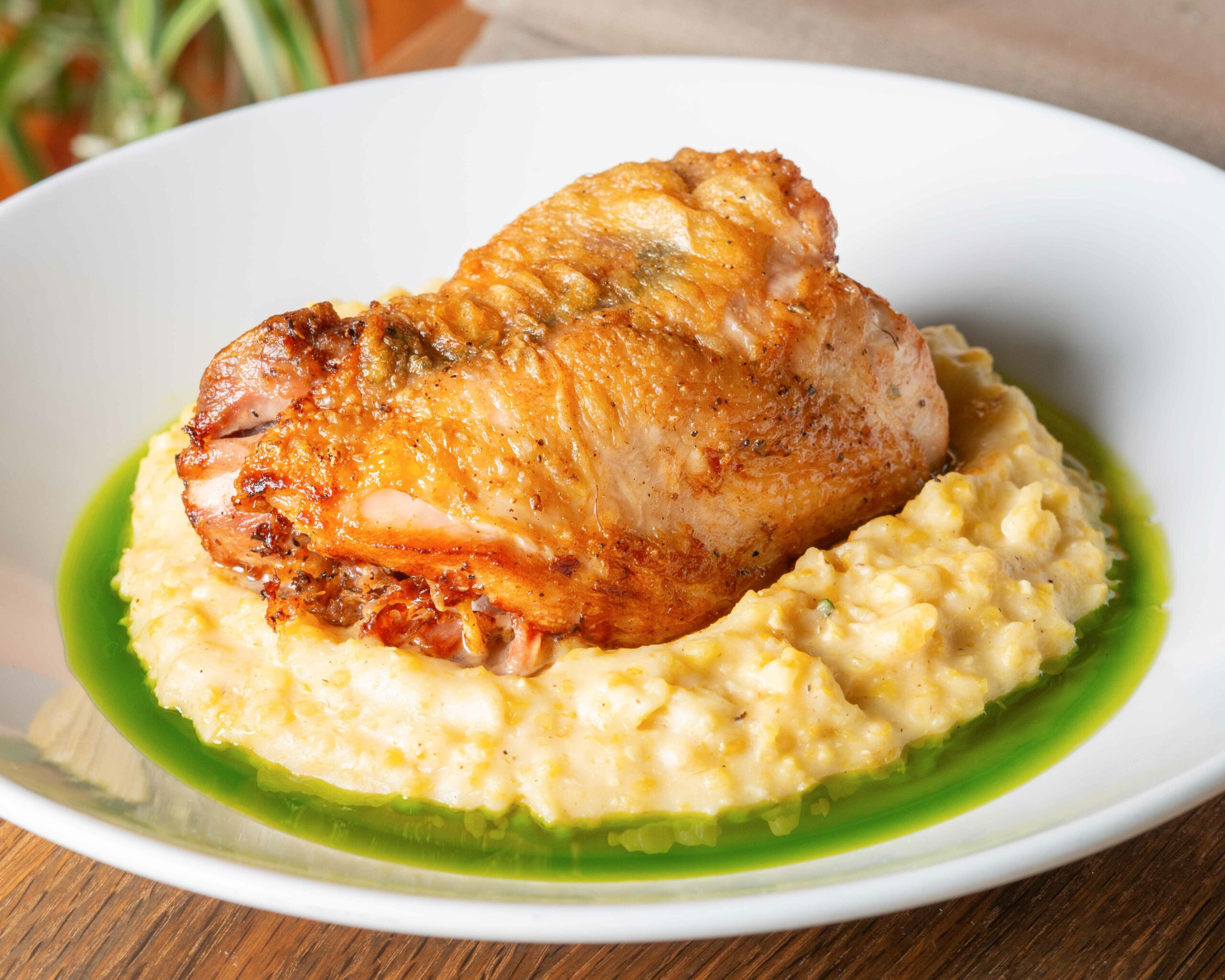 Roasted chicken on a bed of polenta and green sauce on a white sauce.