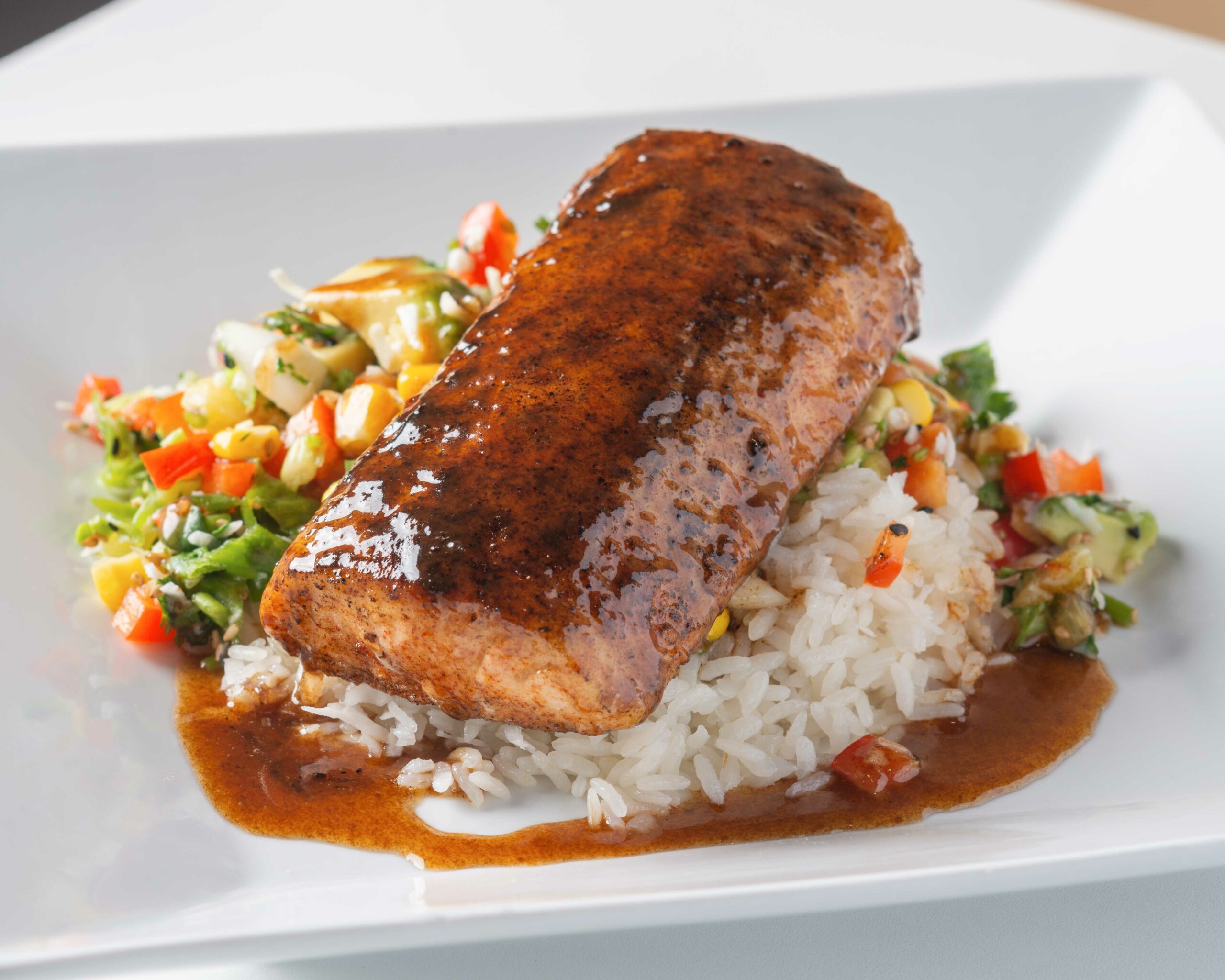 Blackened Mahi-Mahi in a bed of rice and corn salsa on a white plate.