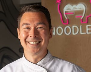 A headshot of Chef Chris Wessely standing in his restaurant, NoodlePig.