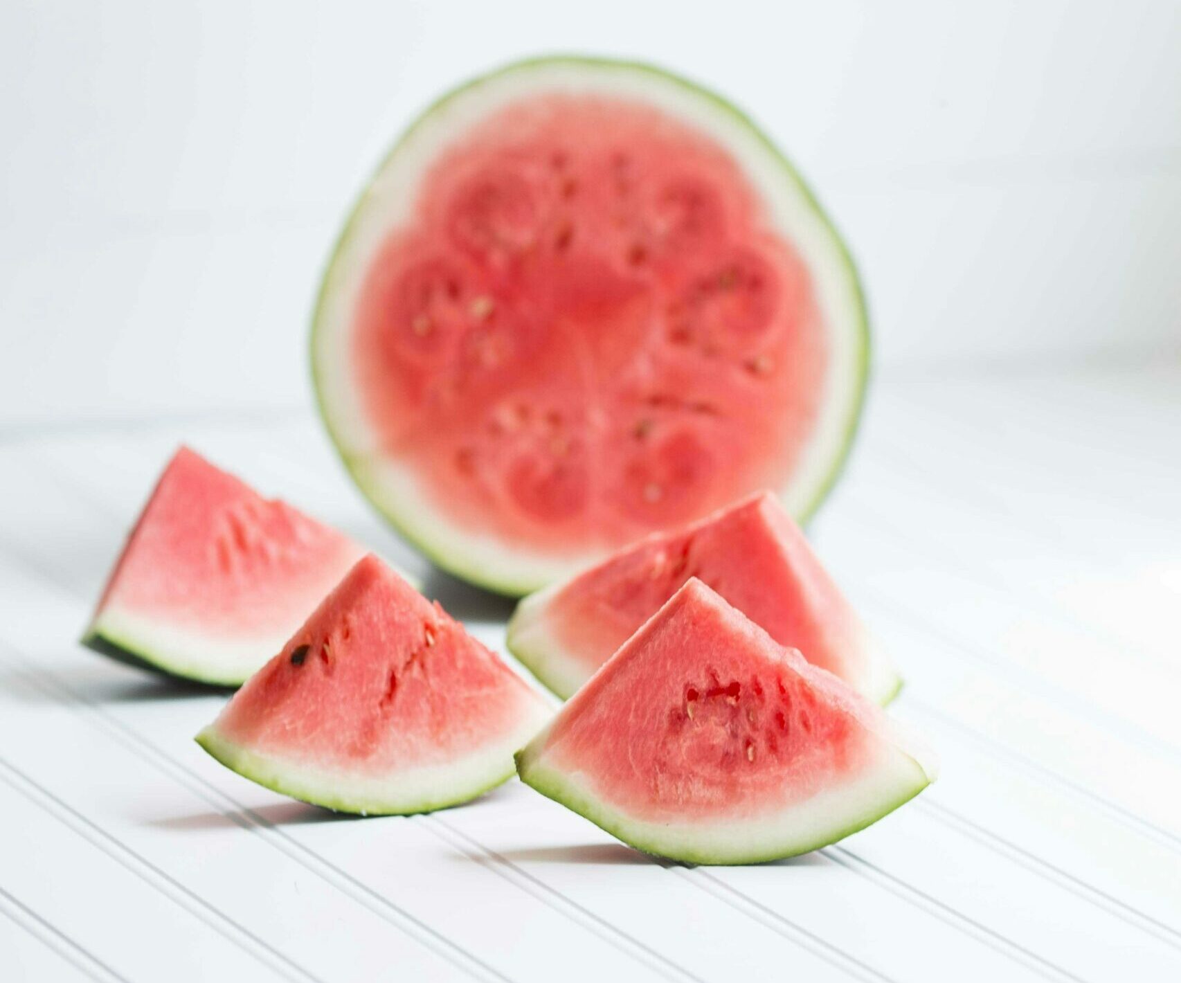 four watermelon slices and a half a watermelon sitting on its side.