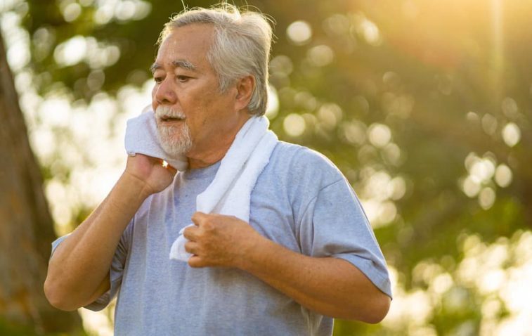 An elderly man after finishing a workout and he wipes sweat away from his face